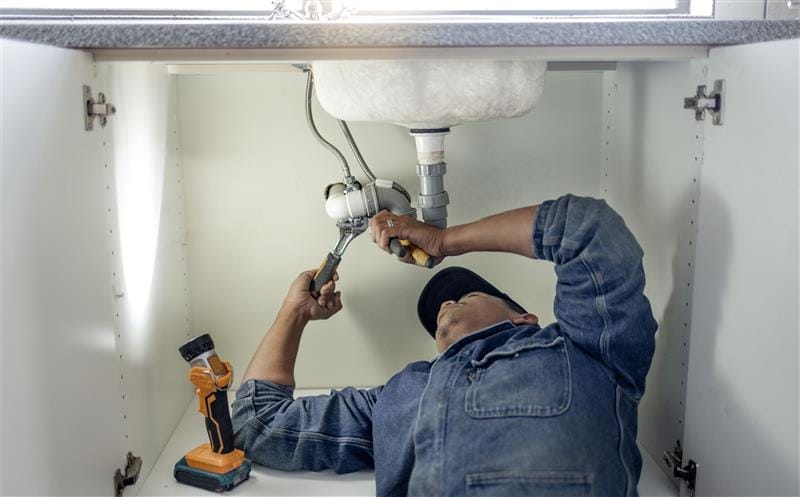 Plumber repairing pipes beneath a bathroom sink in York