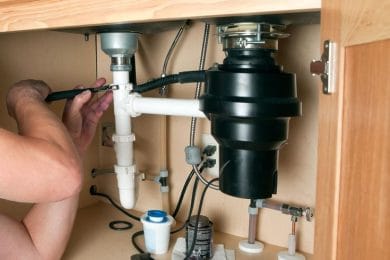 Plumber repairing a garbage disposal beneath a kitchen sink in York